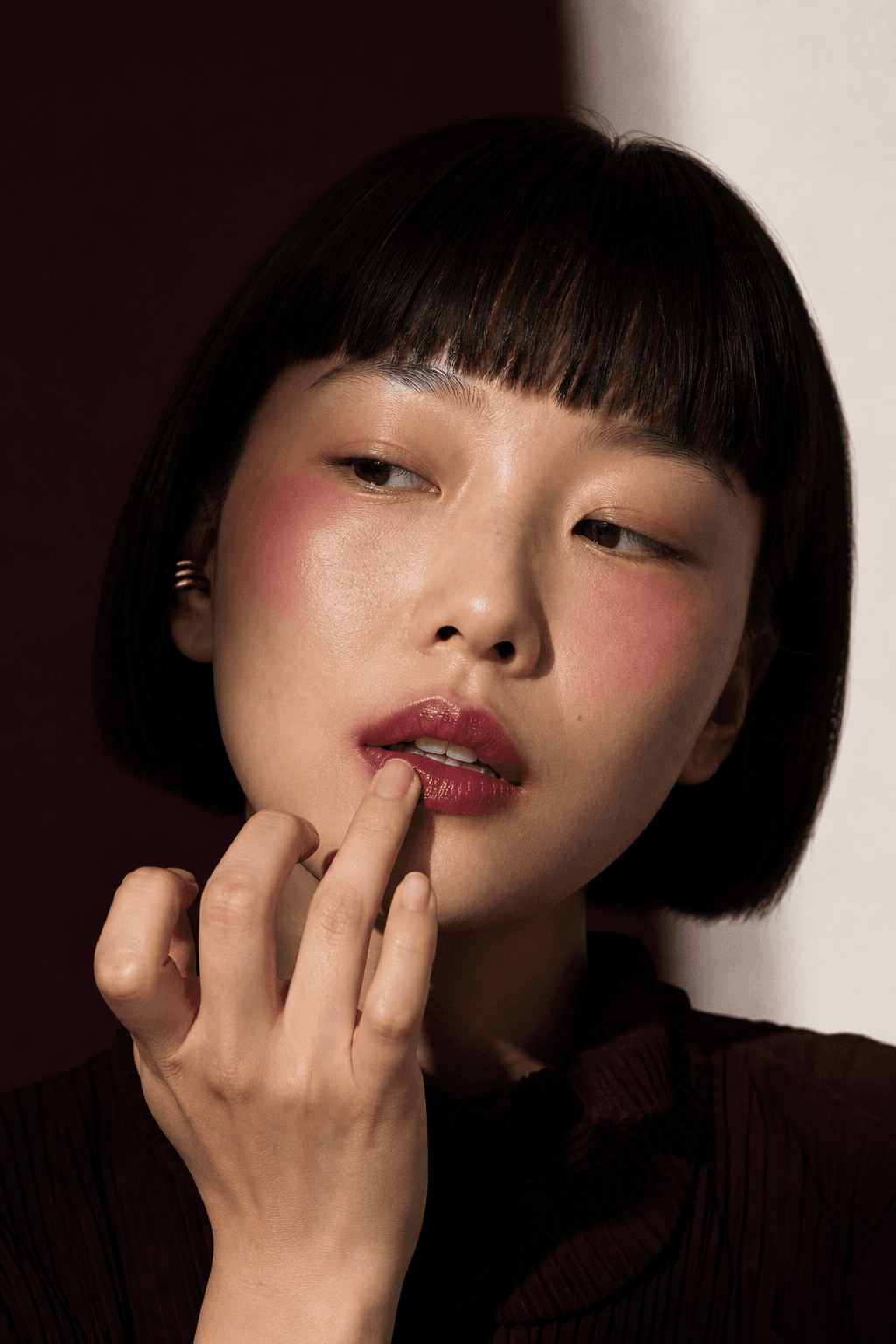 A woman with a short black bob applying lip color with her fingertip.
