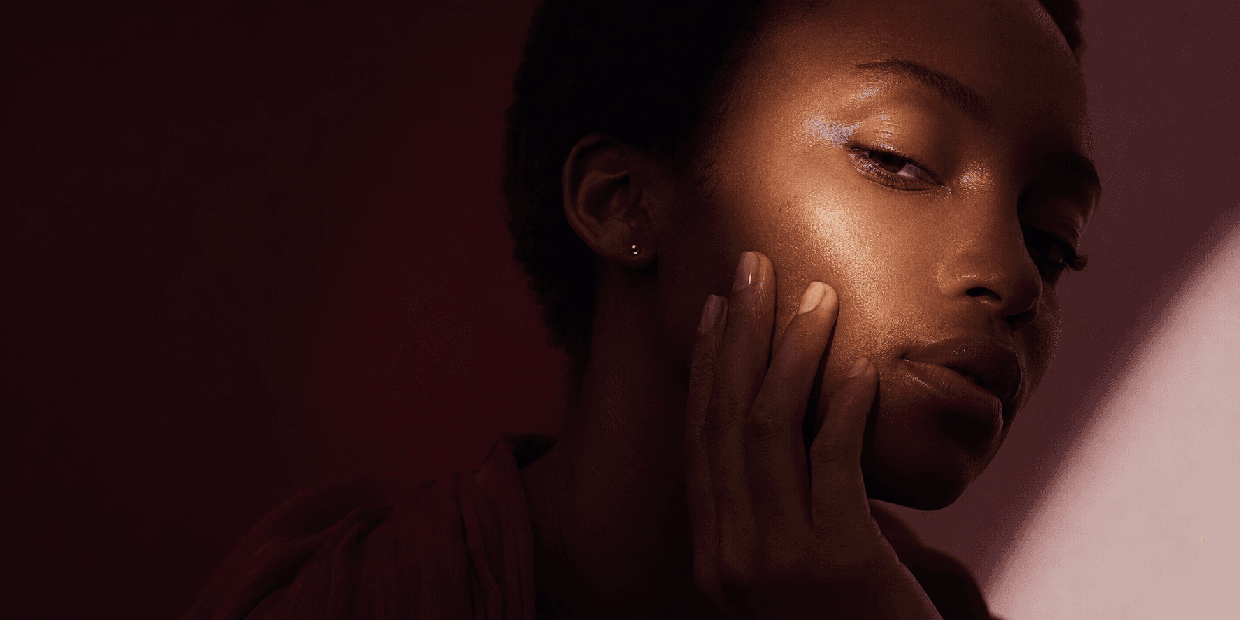 A woman resting her hand softly against her cheek in warm light.